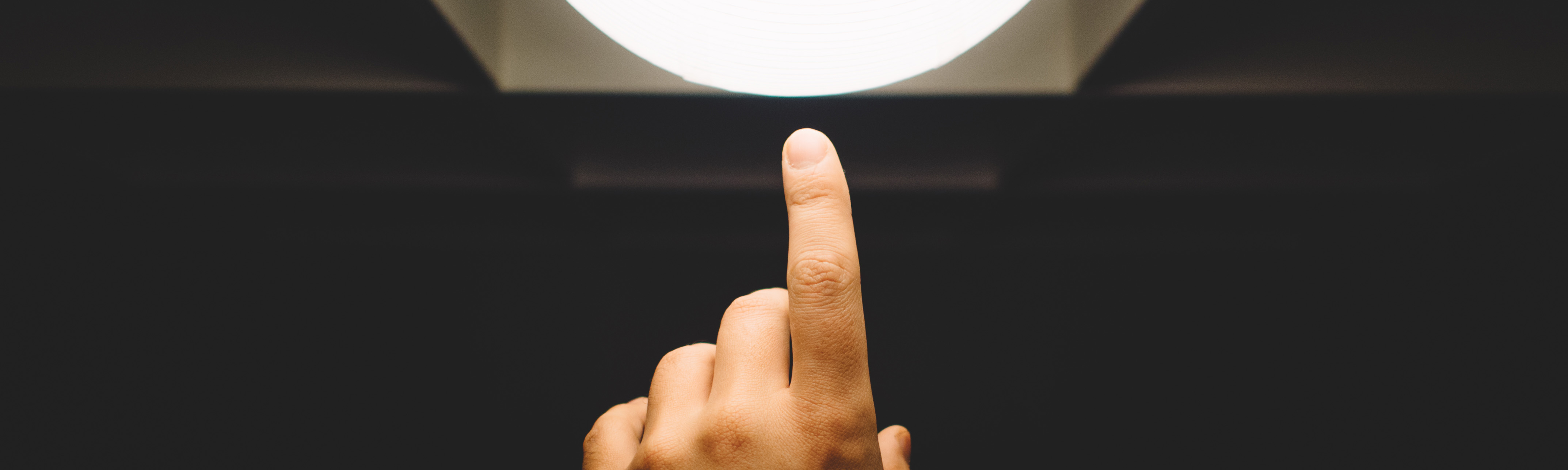Finger pointing at a light-bulb in a darkened room, suggesting innovation.